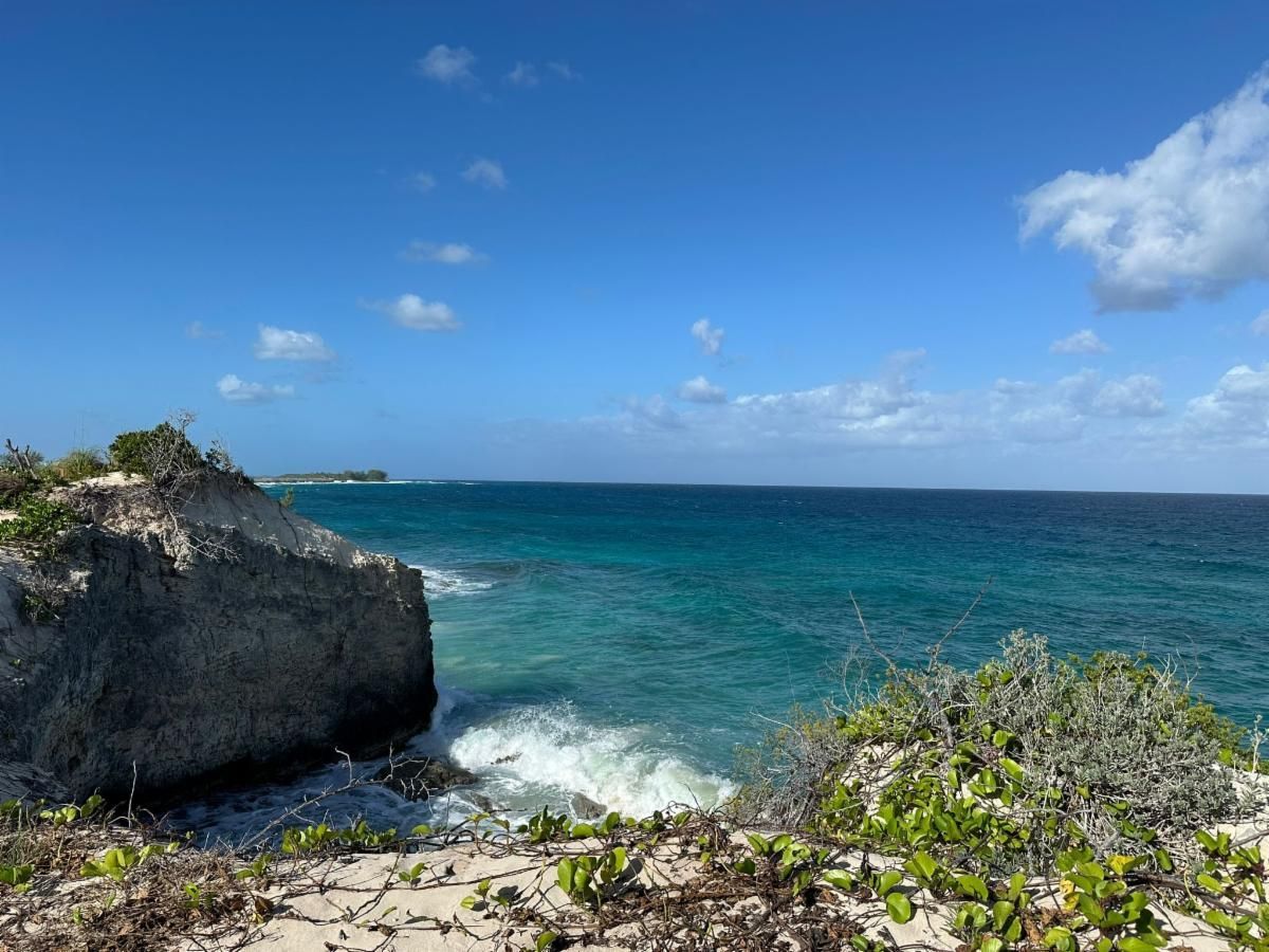 Ocean waves crashing against rocky shoreline under a bright blue sky with white clouds.