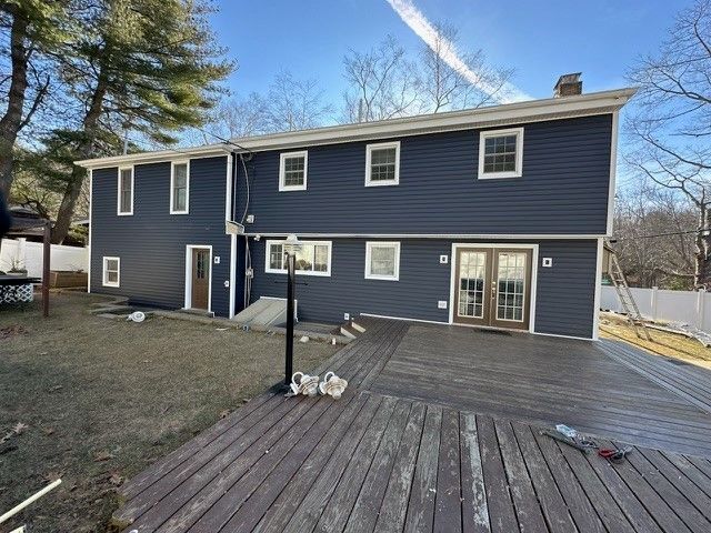 Backyard view of a dark blue two-story house with a large wooden deck and patio doors