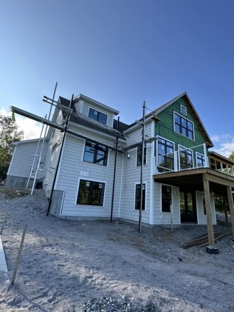 Two-story house under construction with green gables, white siding, and scaffolding on a gravel lot.