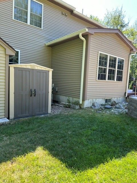 Side view of a house with beige siding, a small storage shed, and a grassy yard in sunlight