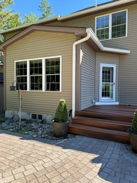 Tan house exterior with white trim, front steps, large windows, and a paved driveway under a blue sky