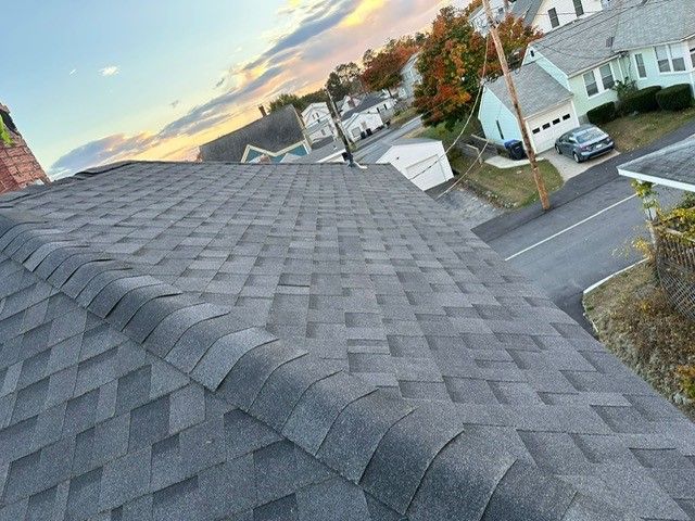Rooftop view of gray shingles overlooking a suburban neighborhood at sunset