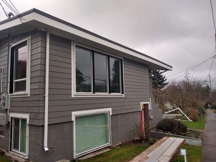 Crisp Gray two-story house exterior with large windows, overcast sky, and a small fenced yard