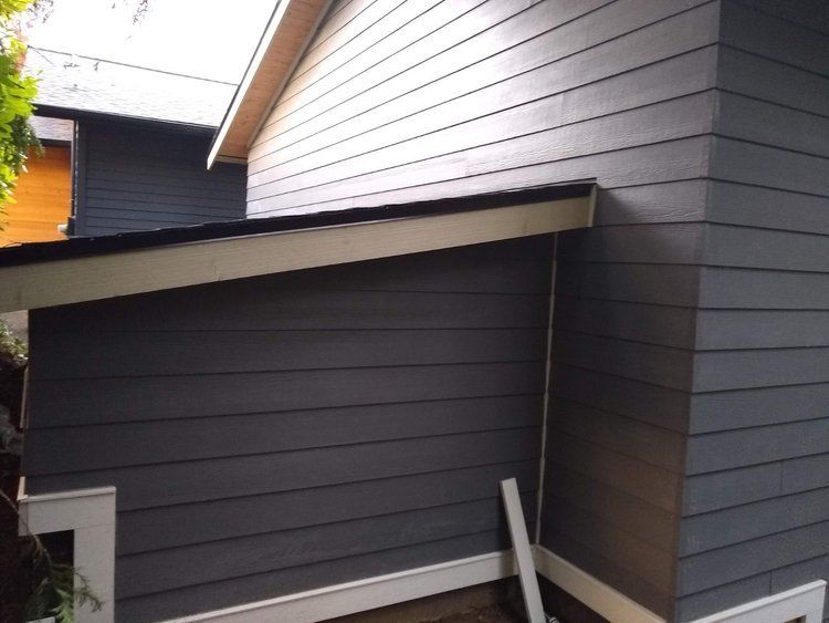 Dark gray house siding and slanted roof over a narrow exterior walkway.
