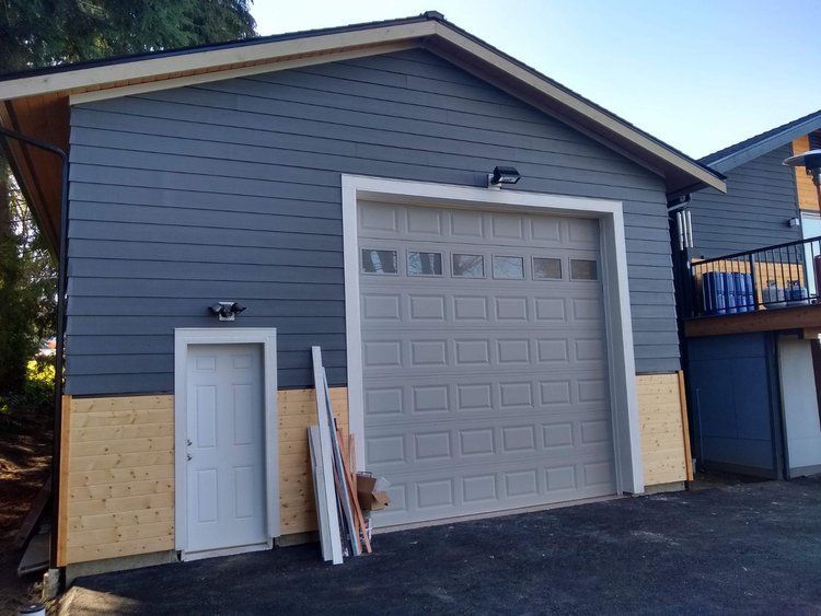 A garage with large white door, white side entry door, and two tone look featured fresh blue siding and yellow foundation