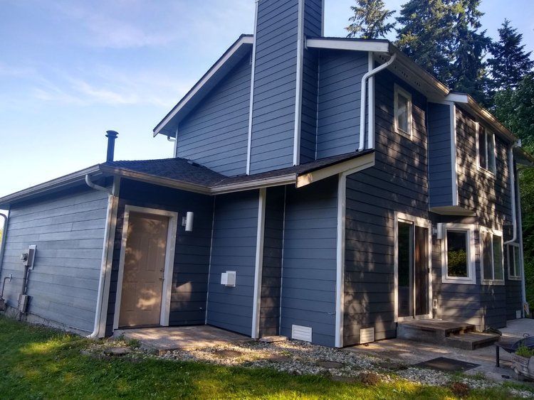 Blue-gray two-story house with a covered porch and unfinished exterior trim under a bright sky