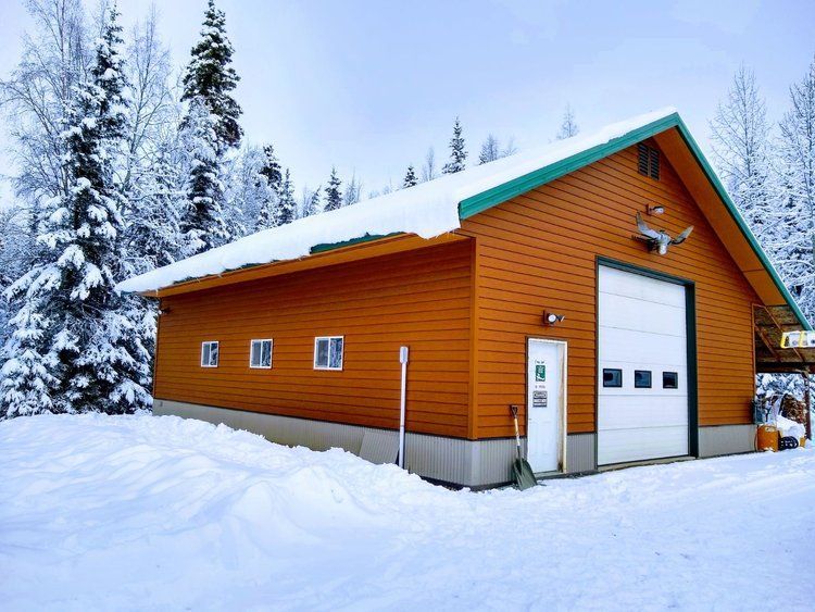Snow-covered orange garage with white doors and evergreen trees in a winter landscape