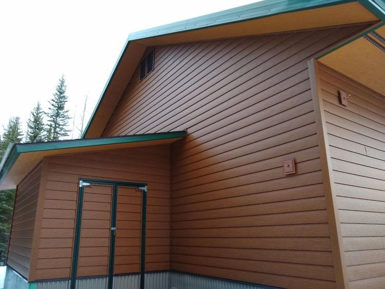 Beautiful new brown siding on a building with a teal-trimmed roof and small porch, viewed from outside.