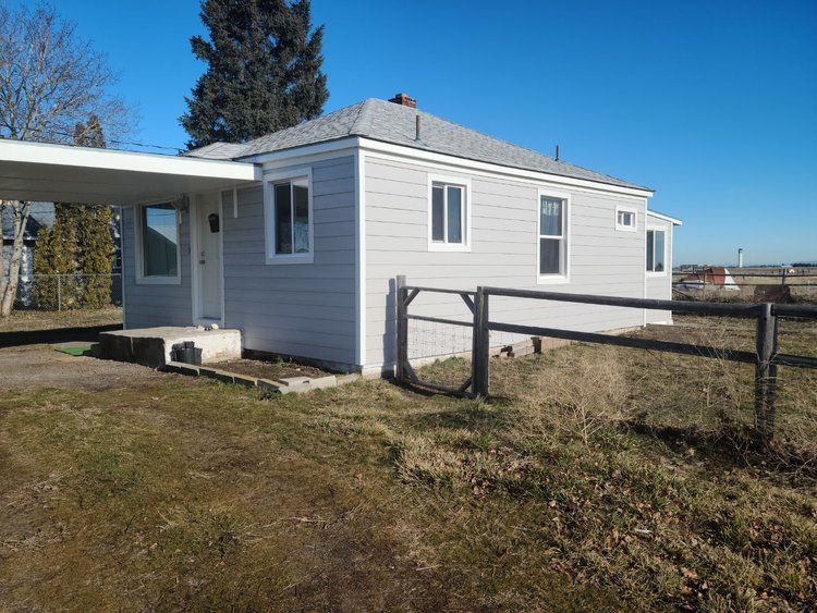 New white siding on a house with a carport, fenced yard, and a clear blue sky.