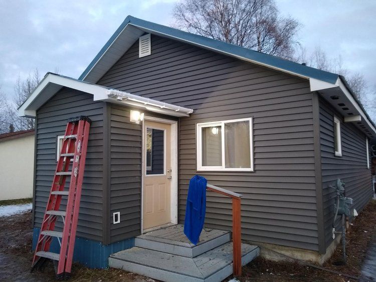 Fresh gray siding of house exterior with a red ladder, porch light on.