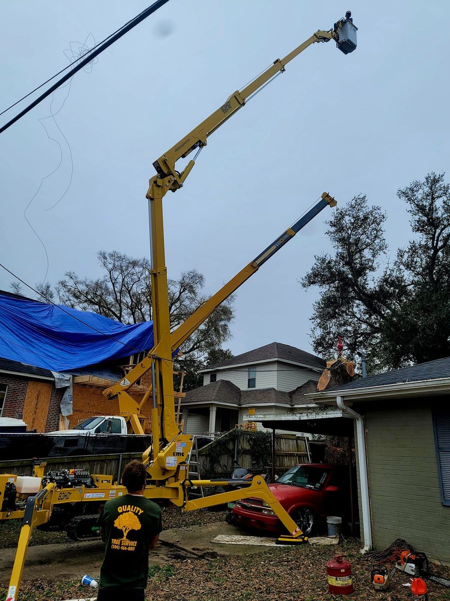 A yellow bucket truck extended into the air over a residential yard, with a person standing nearby.