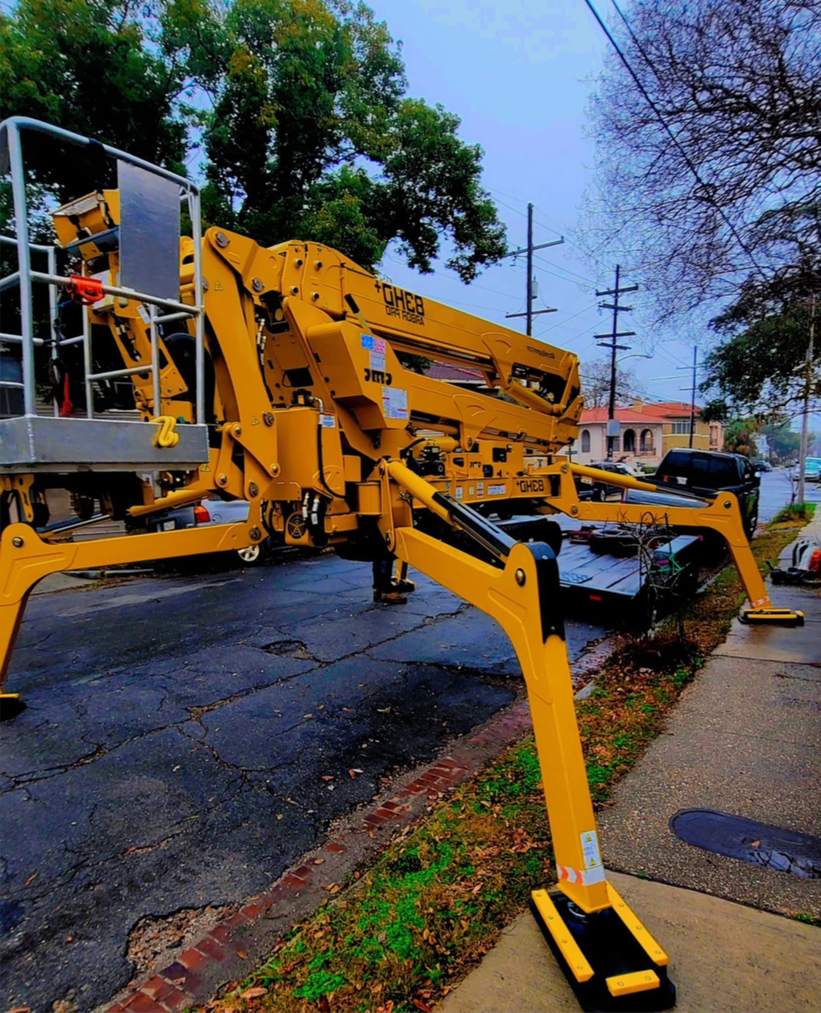 A yellow cherry picker lift with extended outriggers sits on a suburban street in a residential neighborhood.