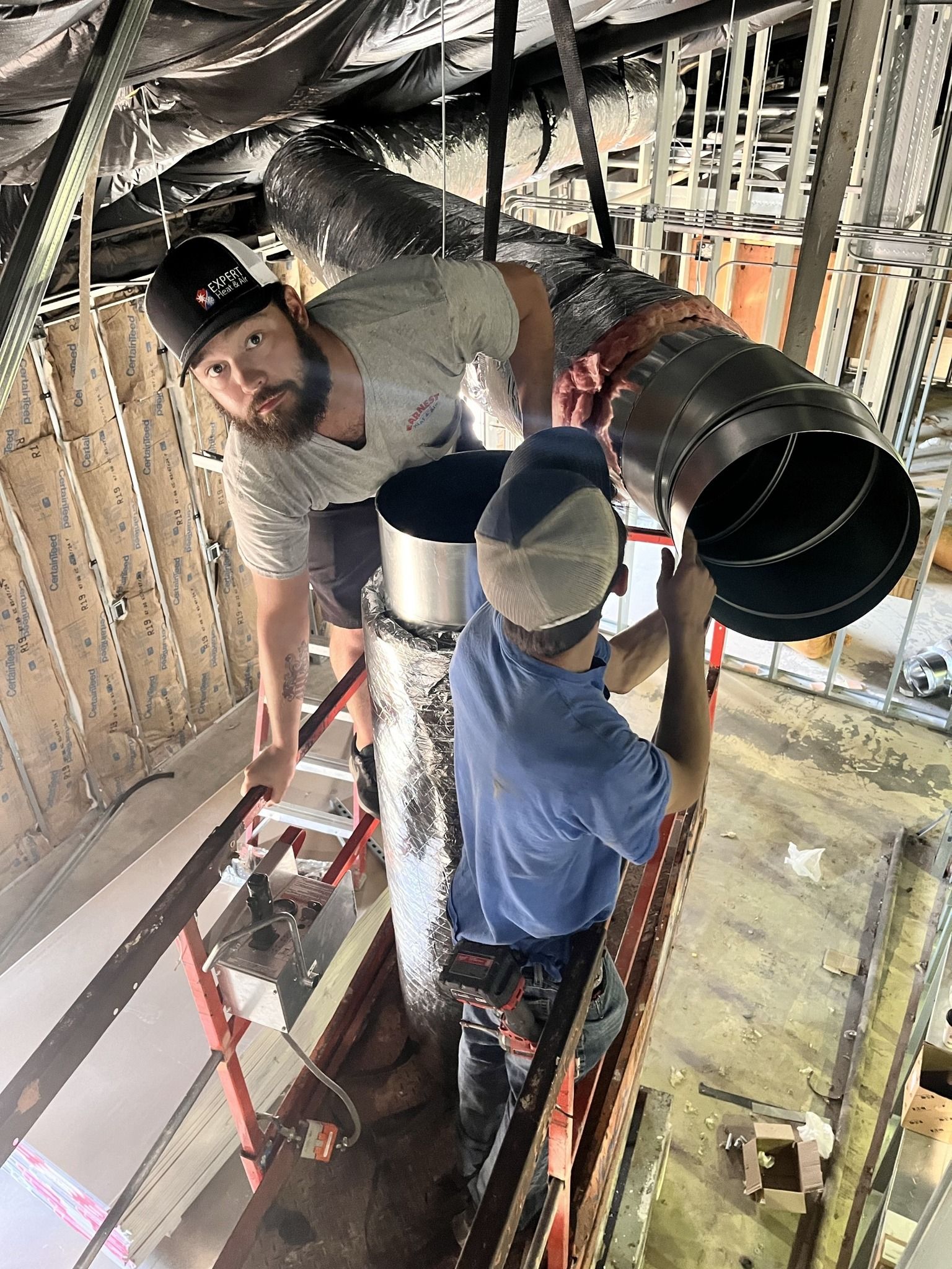 Two men are working on a pipe in a building.