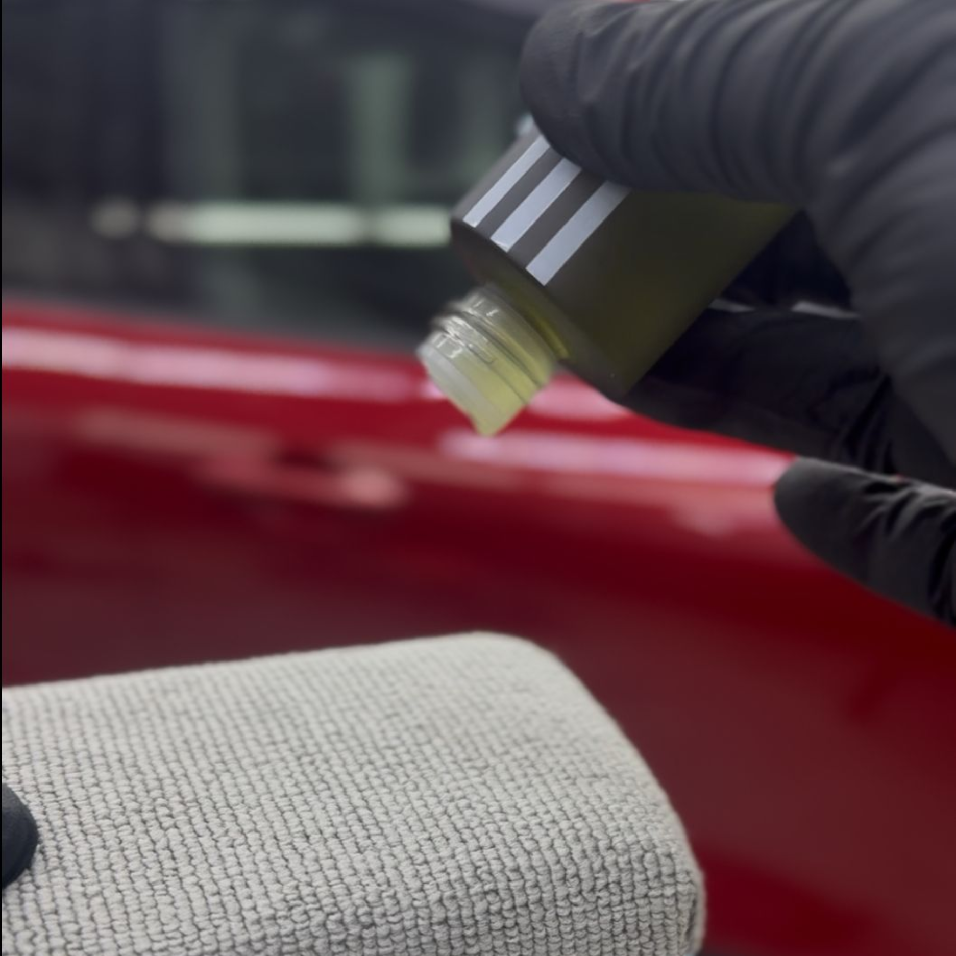 Hands in black gloves applying ceramic coating to car paint.