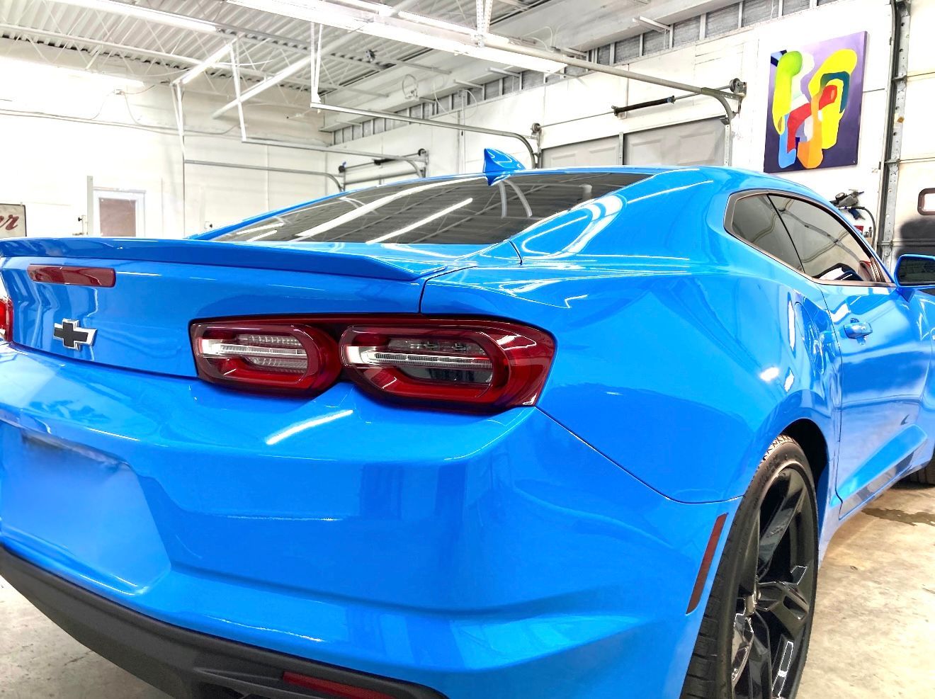Blue Chevrolet Camaro in a bright garage, showcasing glossy paint and black wheels.