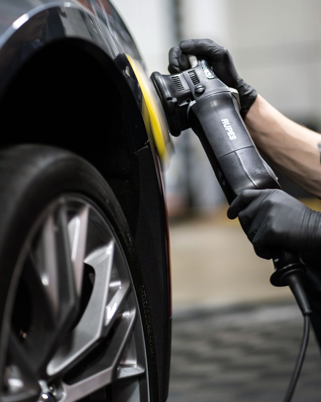 Person polishing a black car fender with a power tool.
