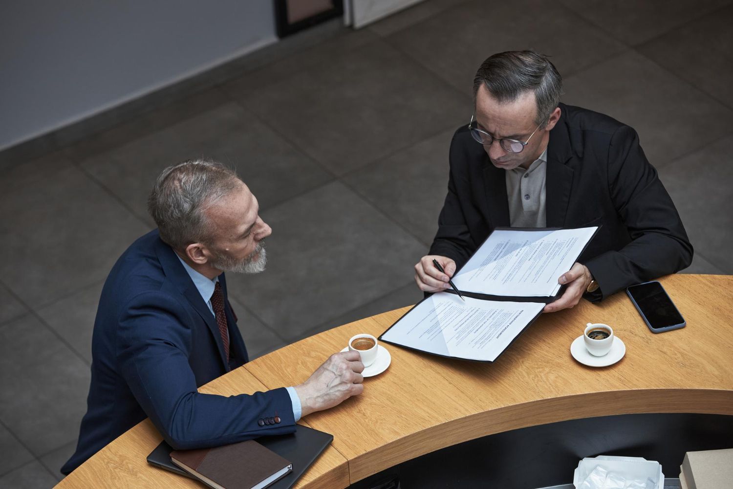 Two business professionals in suits reviewing documents, discussing strategy.