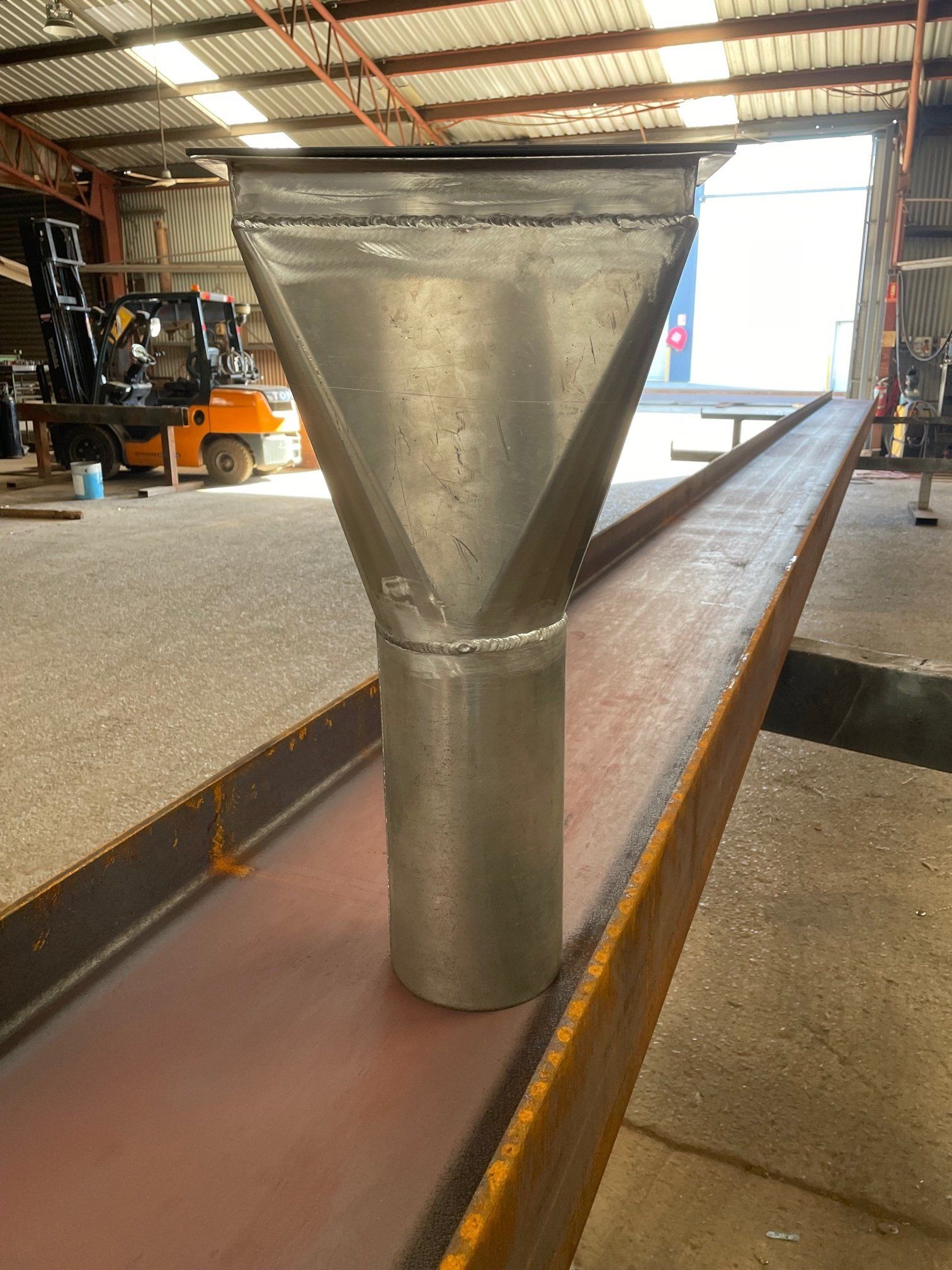 A metal pipe is sitting on top of a metal beam in a warehouse.