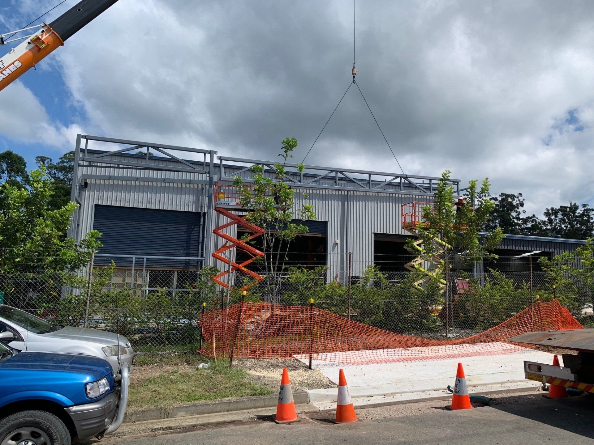 A crane is lifting a tree in front of a building under construction.