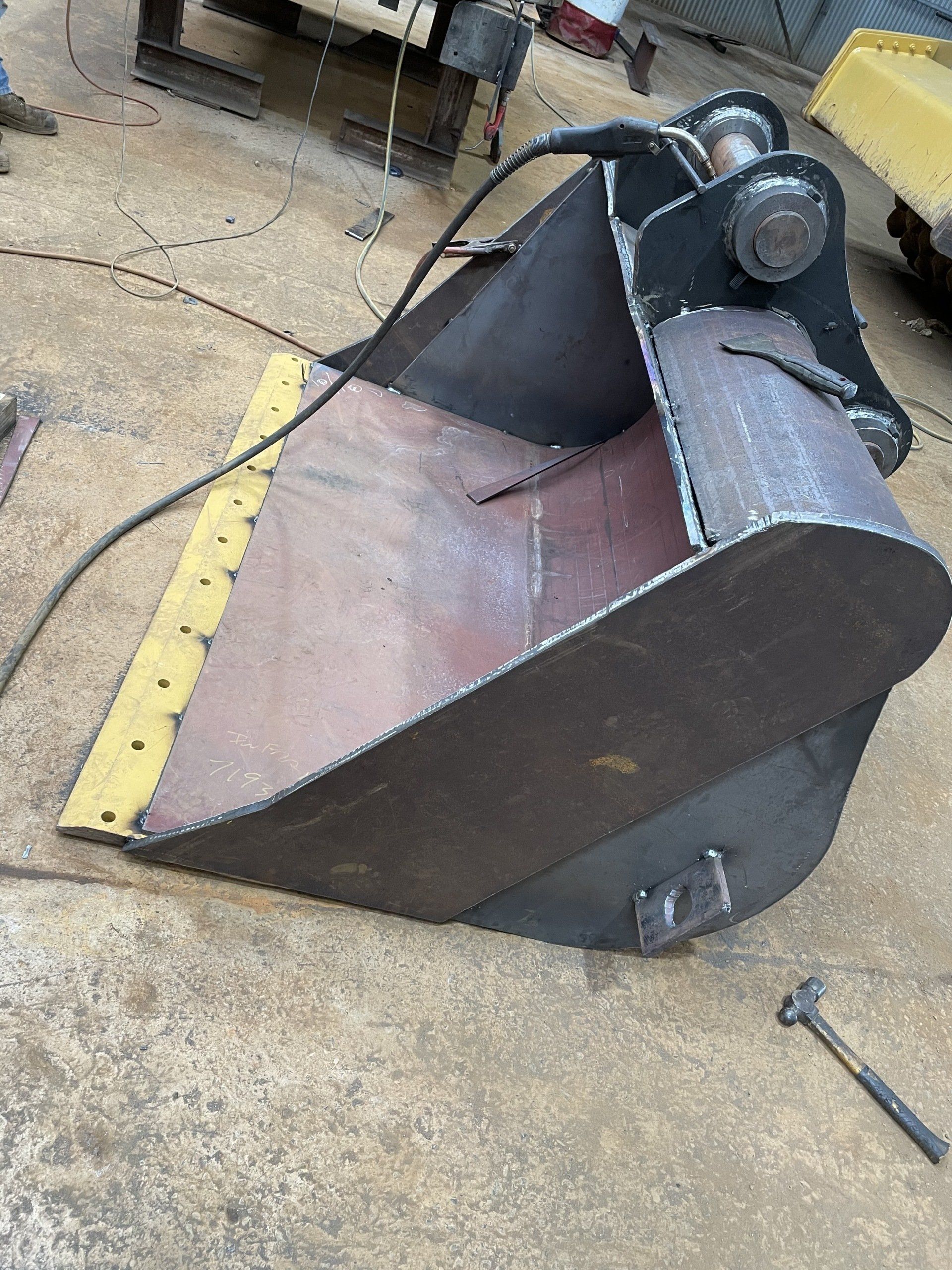 A large metal bucket is sitting on the ground next to a hammer.