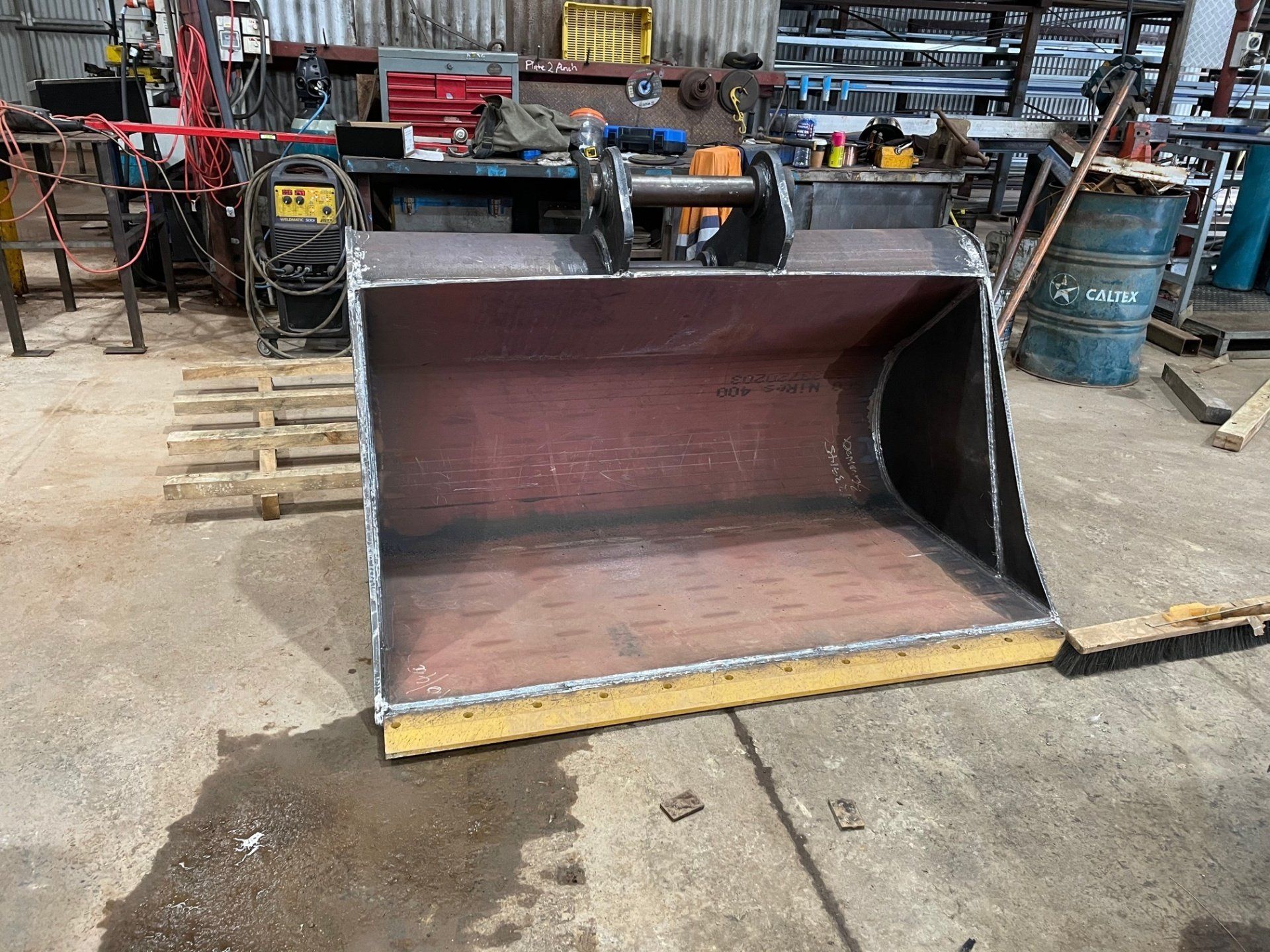 A large metal bucket is sitting on the ground in a garage.