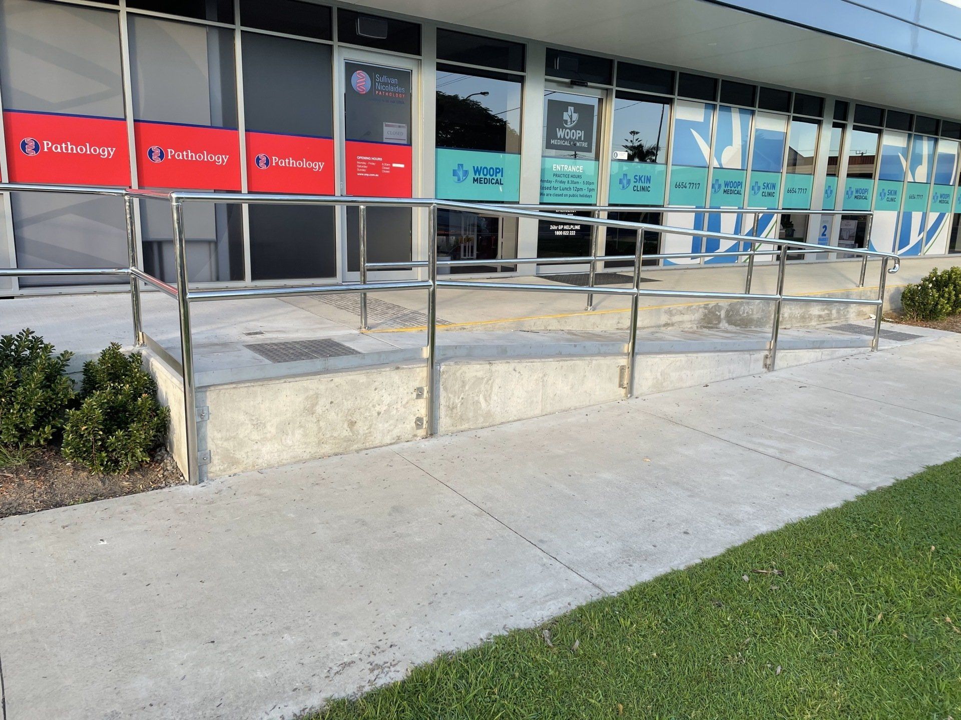 A concrete walkway leading to a building with a stainless steel railing