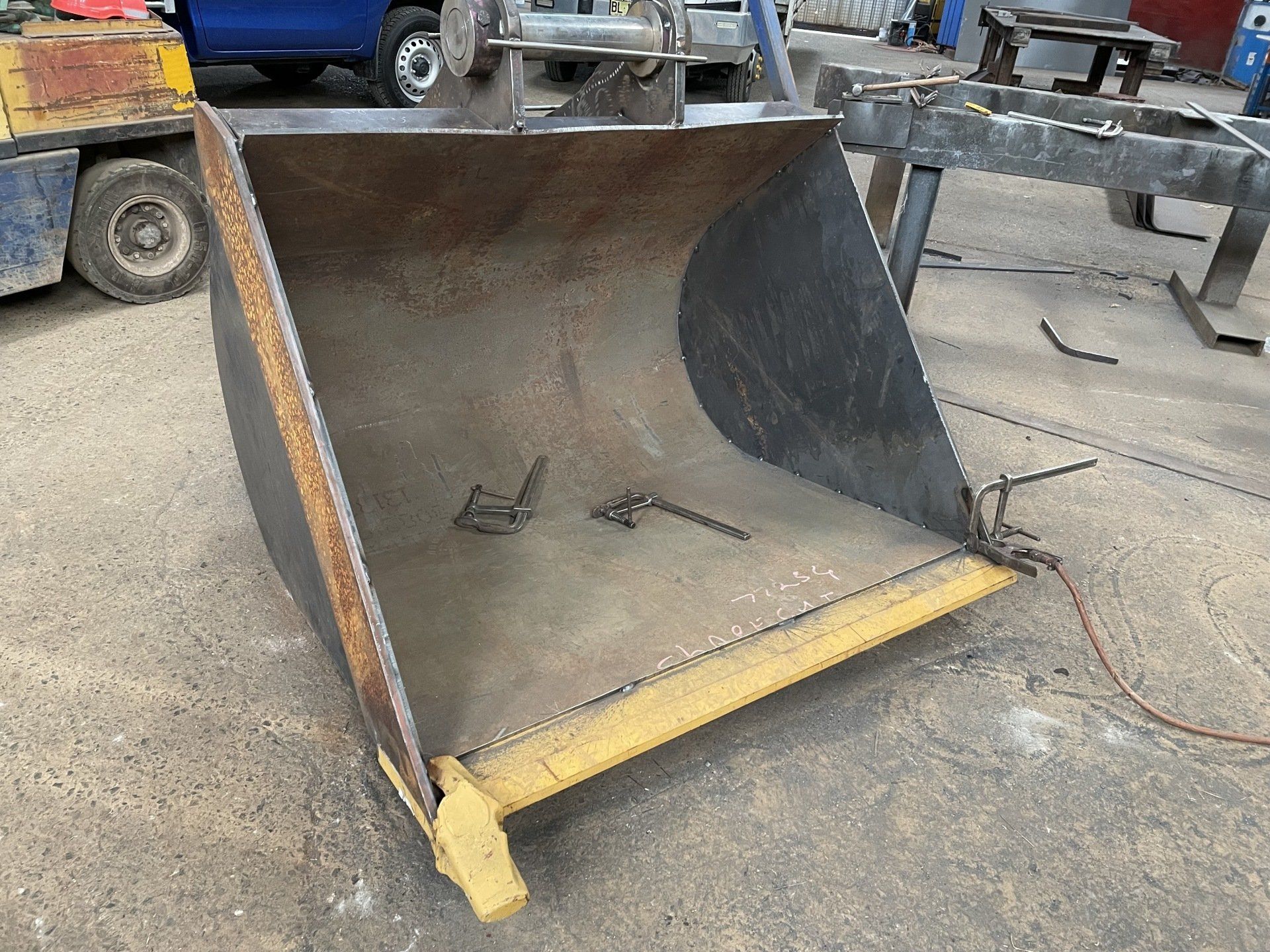A large metal bucket is sitting on the ground next to a forklift.