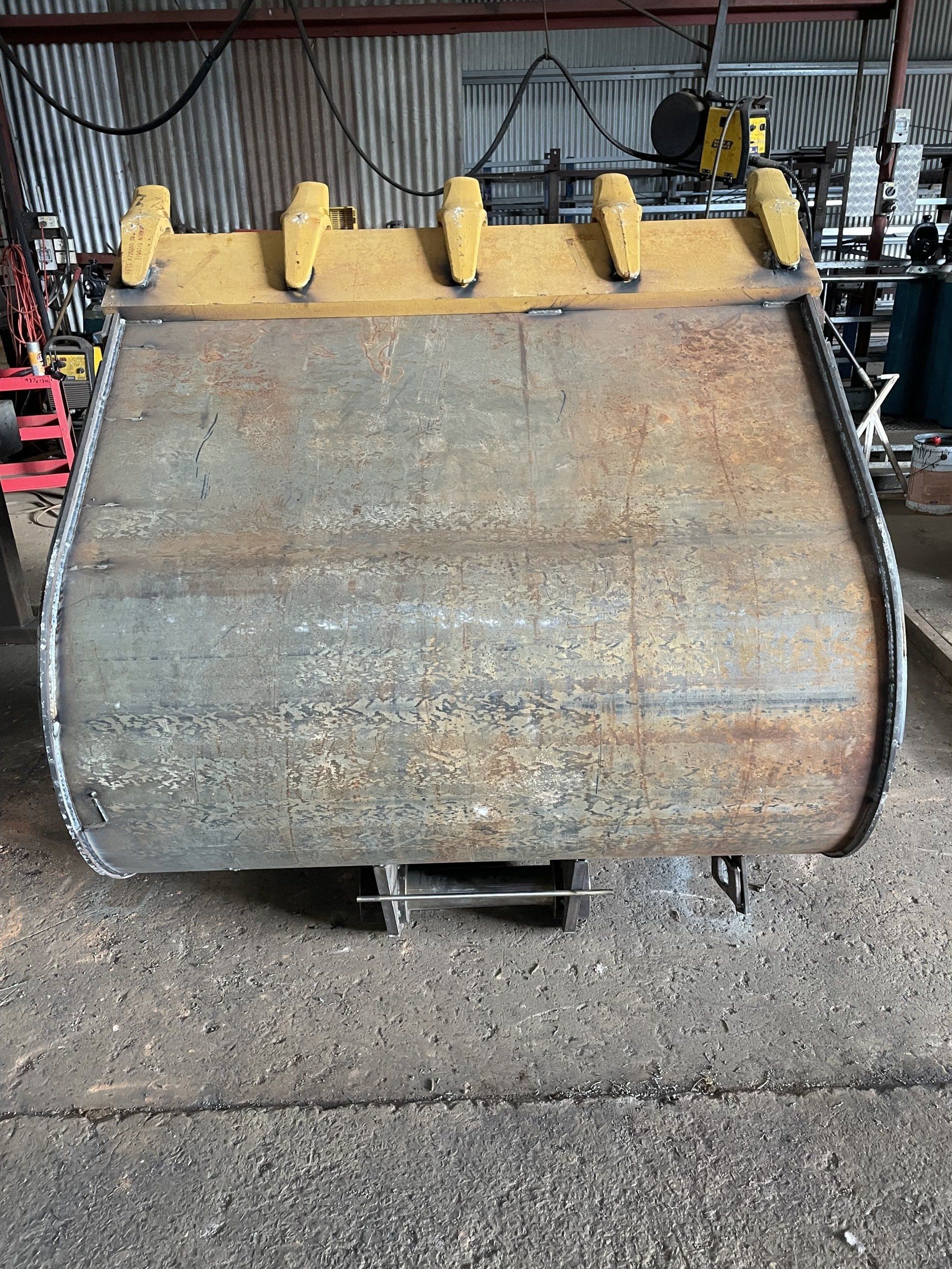 A large metal bucket is sitting on the ground in a garage.
