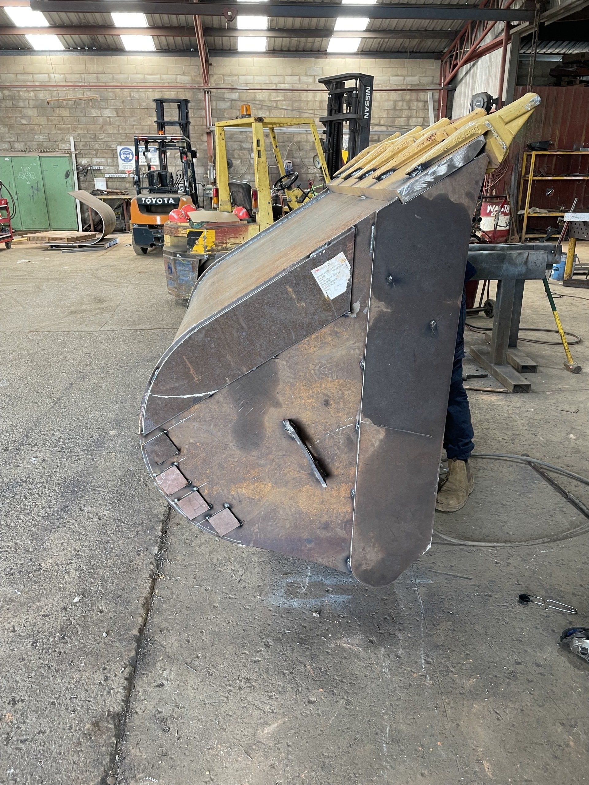 A large metal bucket is sitting on the ground in a warehouse.