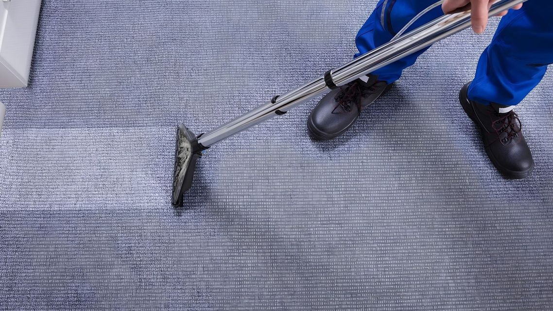 Person scrubbing a large patterned rug on a worktable with soap and water