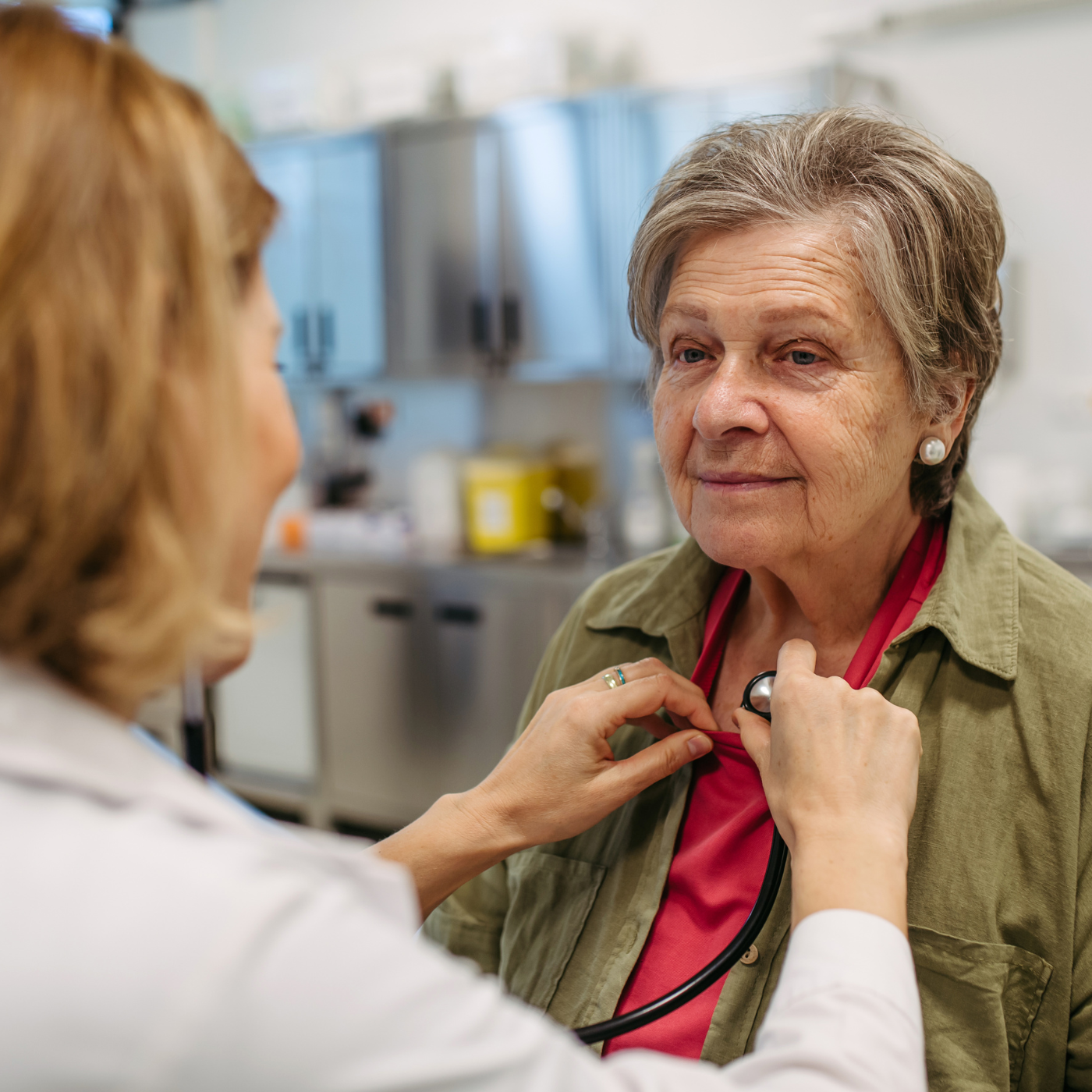 Médico auscultando o tórax de um paciente idoso com um estetoscópio em um ambiente clínico.