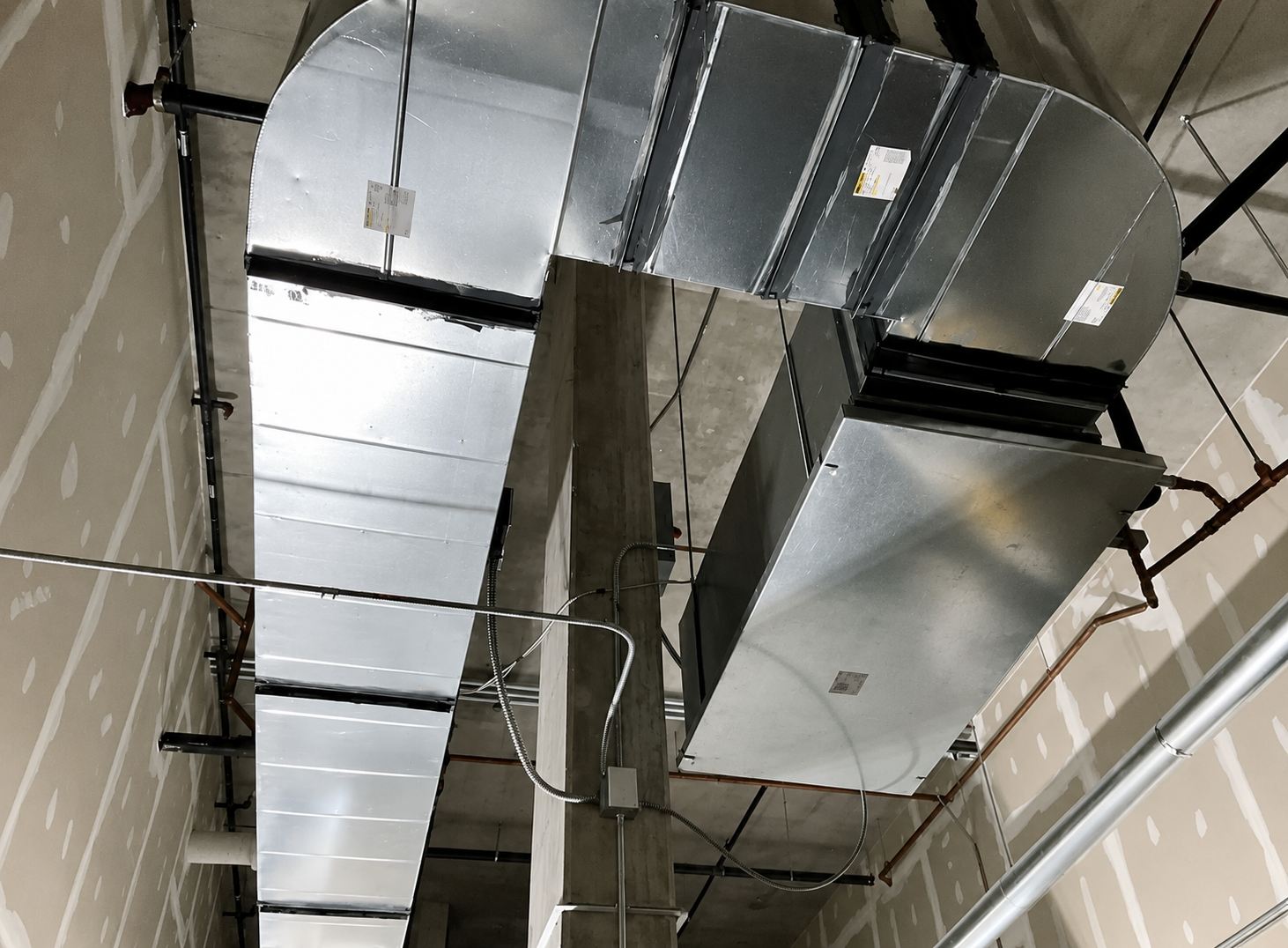 Silver HVAC ductwork mounted on a high ceiling in an unfinished room