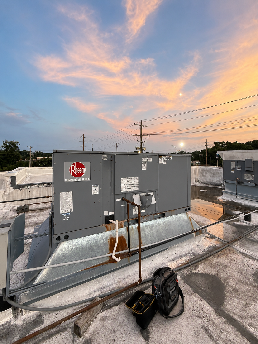 Gray rooftop HVAC units at sunset with pink clouds and a bag on the roof.