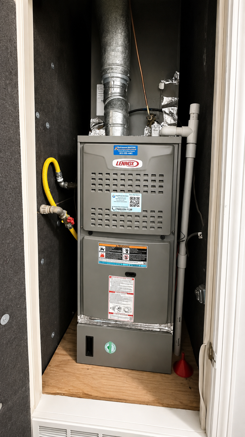 Furnace and HVAC equipment in a small utility closet with exposed ducts and wiring