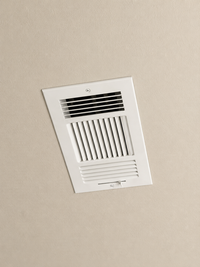 Ceiling-mounted bathroom exhaust vent with white grille on a beige ceiling