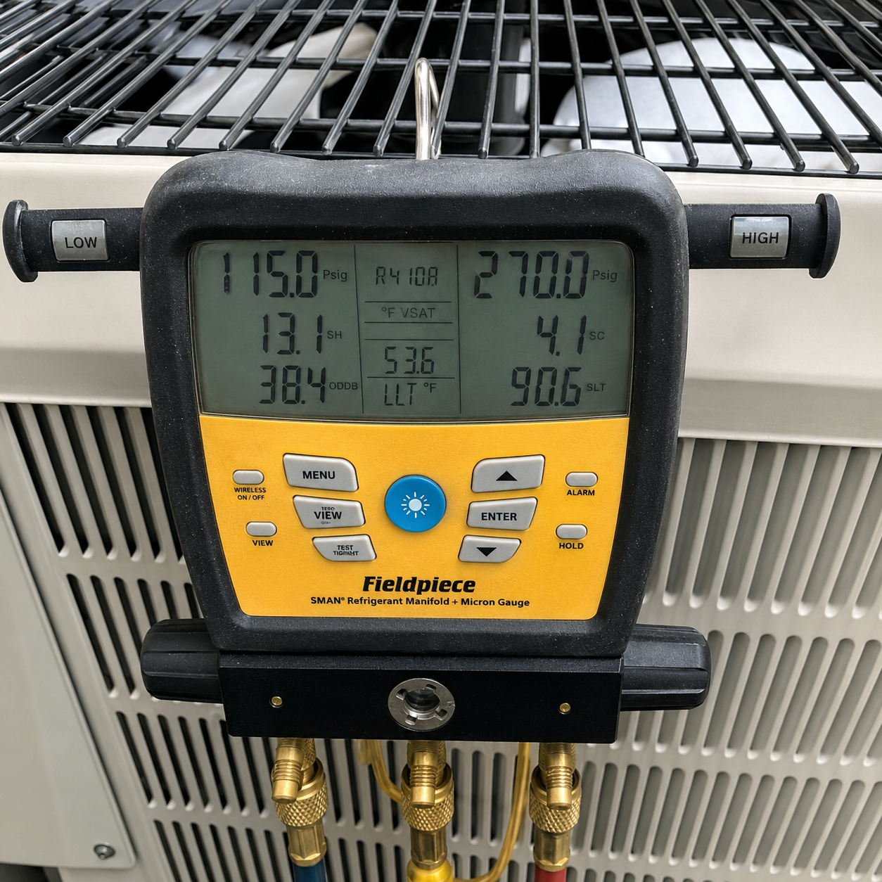 Yellow Fieldpiece HVAC gauge with digital display and brass hoses attached to outdoor unit