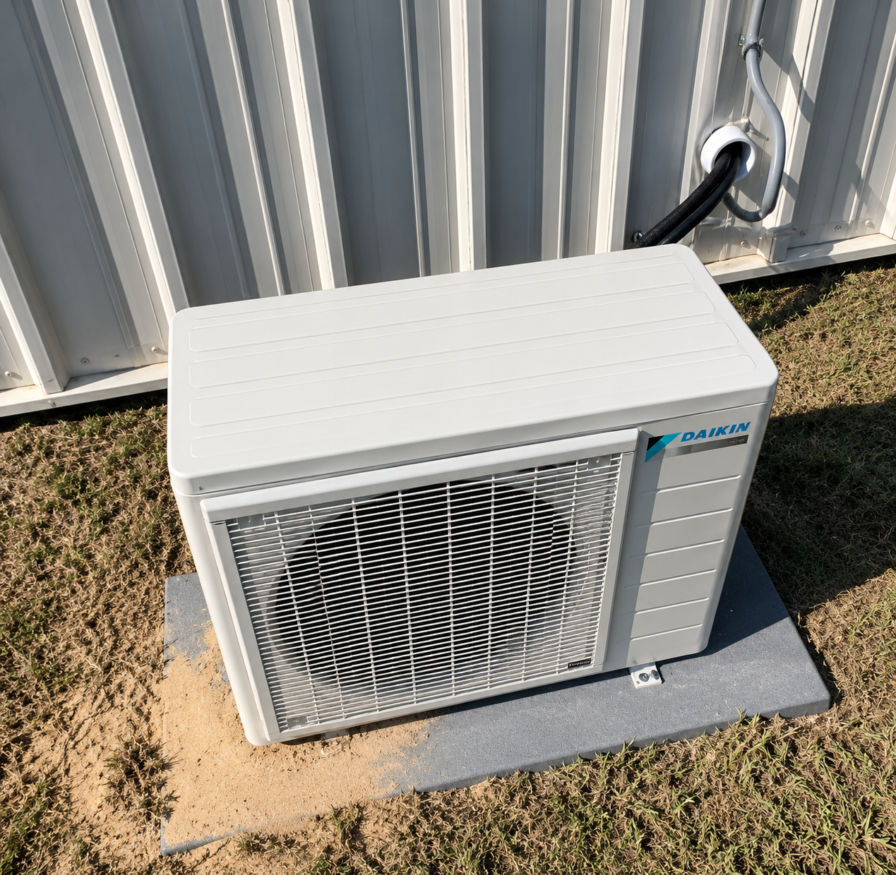 White outdoor air conditioner unit beside a corrugated metal wall on a concrete pad