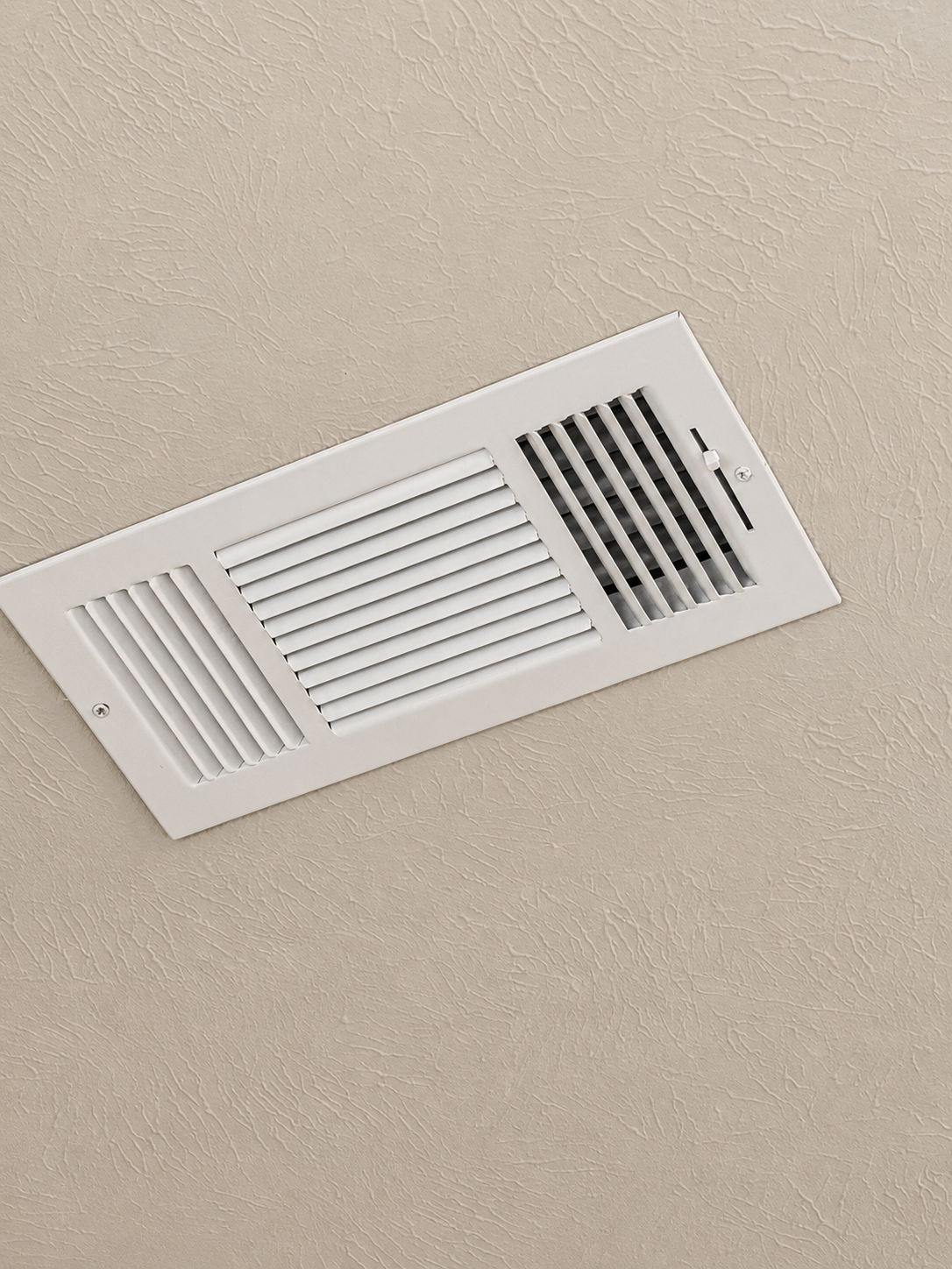 White ceiling air vent with rectangular grilles against a beige ceiling