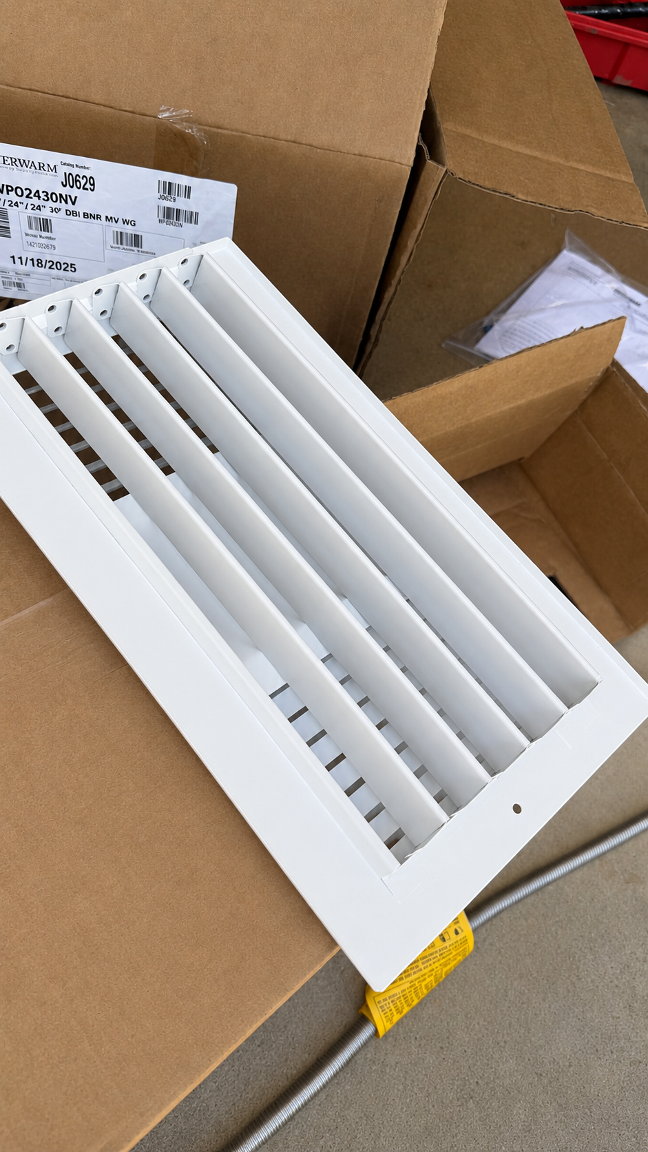 White vent grille resting in an open cardboard box on a floor.