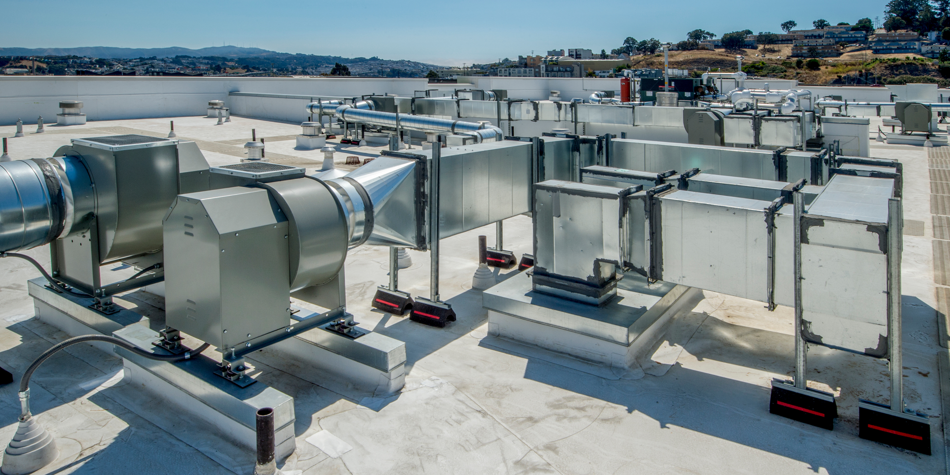 Rooftop HVAC ductwork and ventilation equipment on a flat industrial roof with city and water in the distance