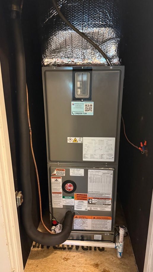 Indoor HVAC furnace unit in a closet, with black insulated ducts and a small control panel.