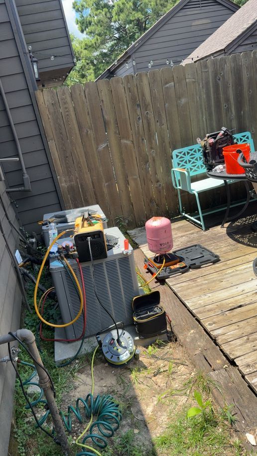 Backyard with a wooden deck, fence, outdoor chairs, and scattered tools and hoses beside a house.