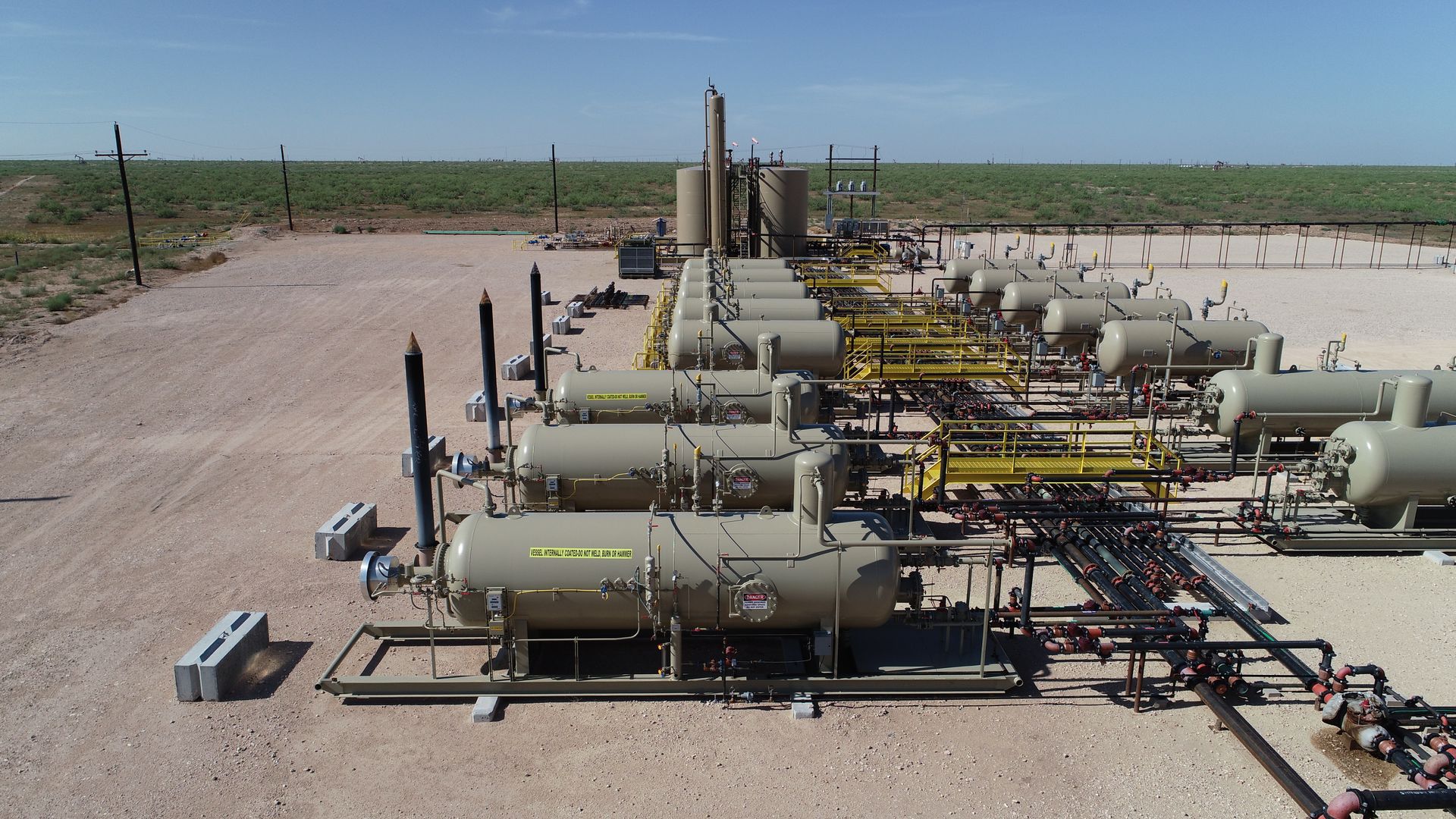 A row of tanks and pipes are lined up in a field.