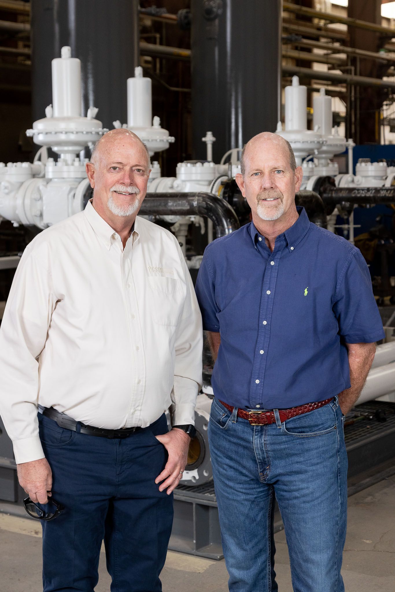 Two brothers are standing next to each other in front of a machine in a factory.