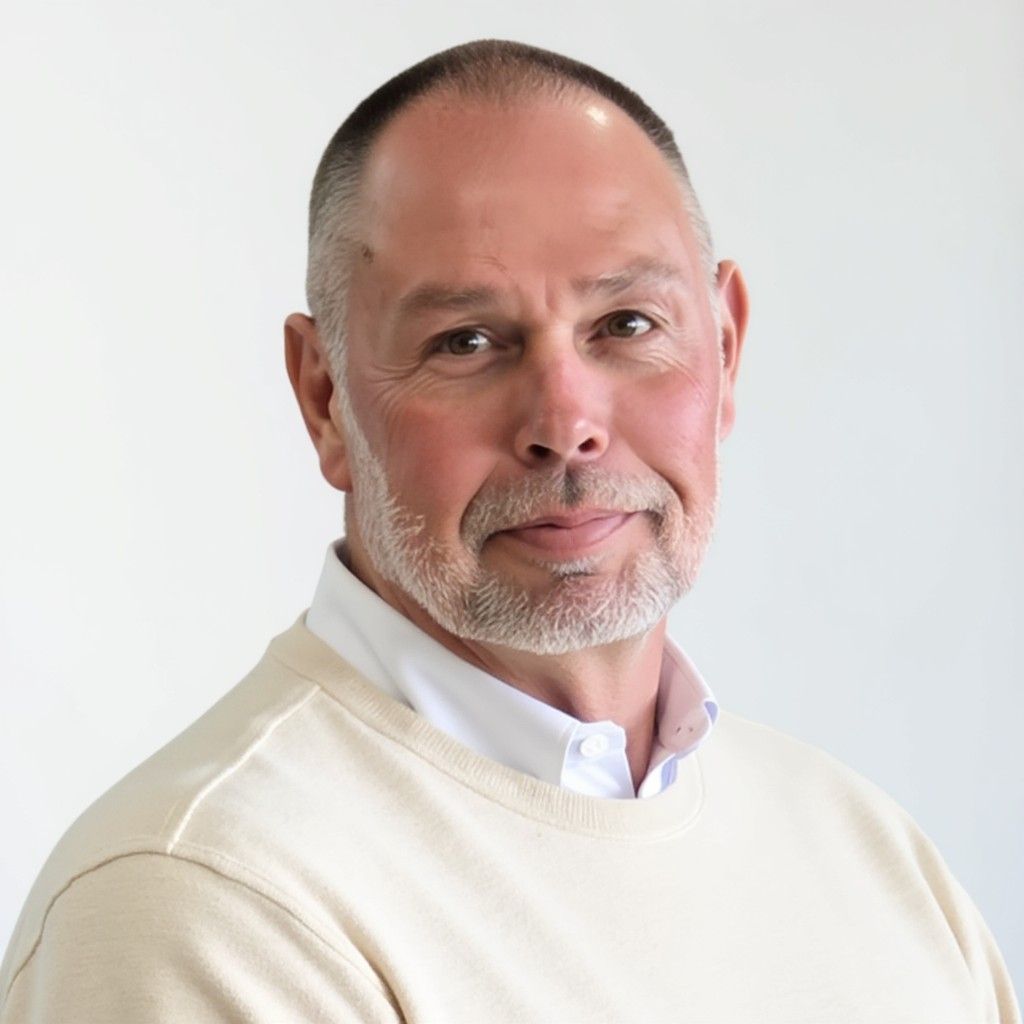 Portrait of a man in a cream sweater and white shirt against a light gray background