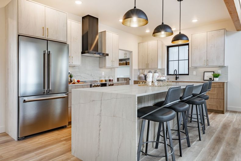 Modern kitchen with white cabinets, stainless steel fridge, marble island, and black bar stools under pendant lights