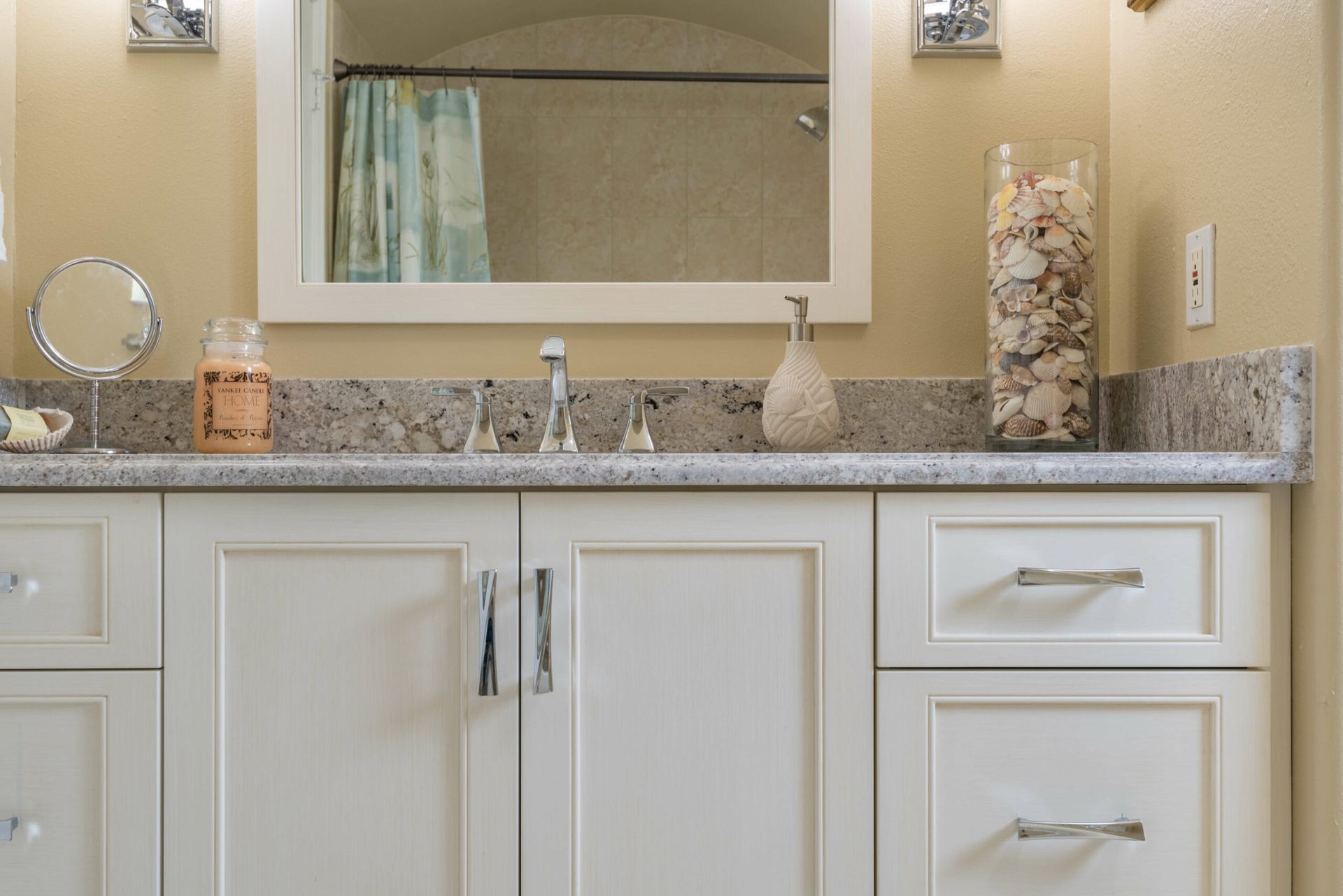 Bathroom vanity with granite countertop, mirror, sink, and decorative accessories.