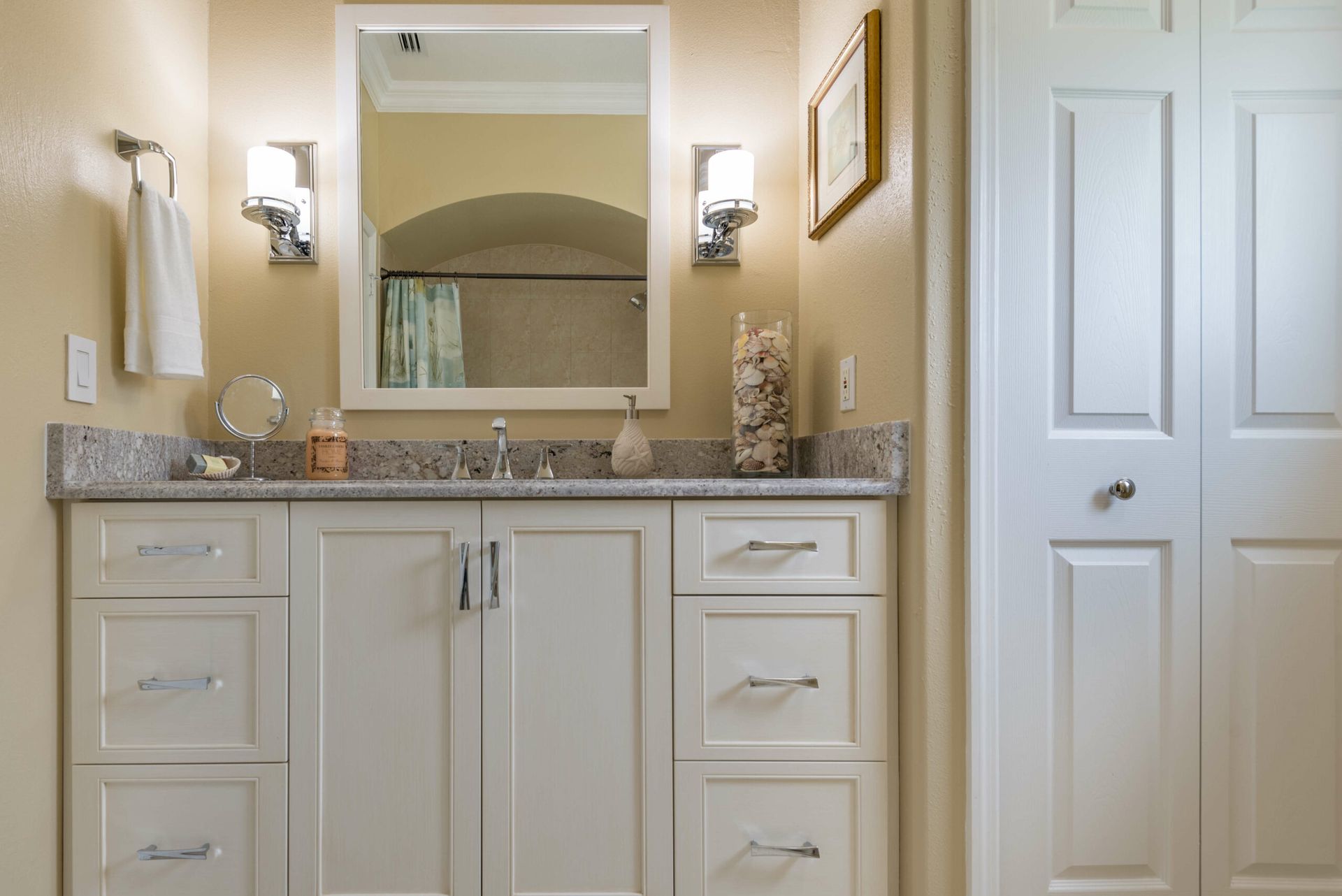 White bathroom vanity with mirror, sink, wall sconce, and closed door beside it.