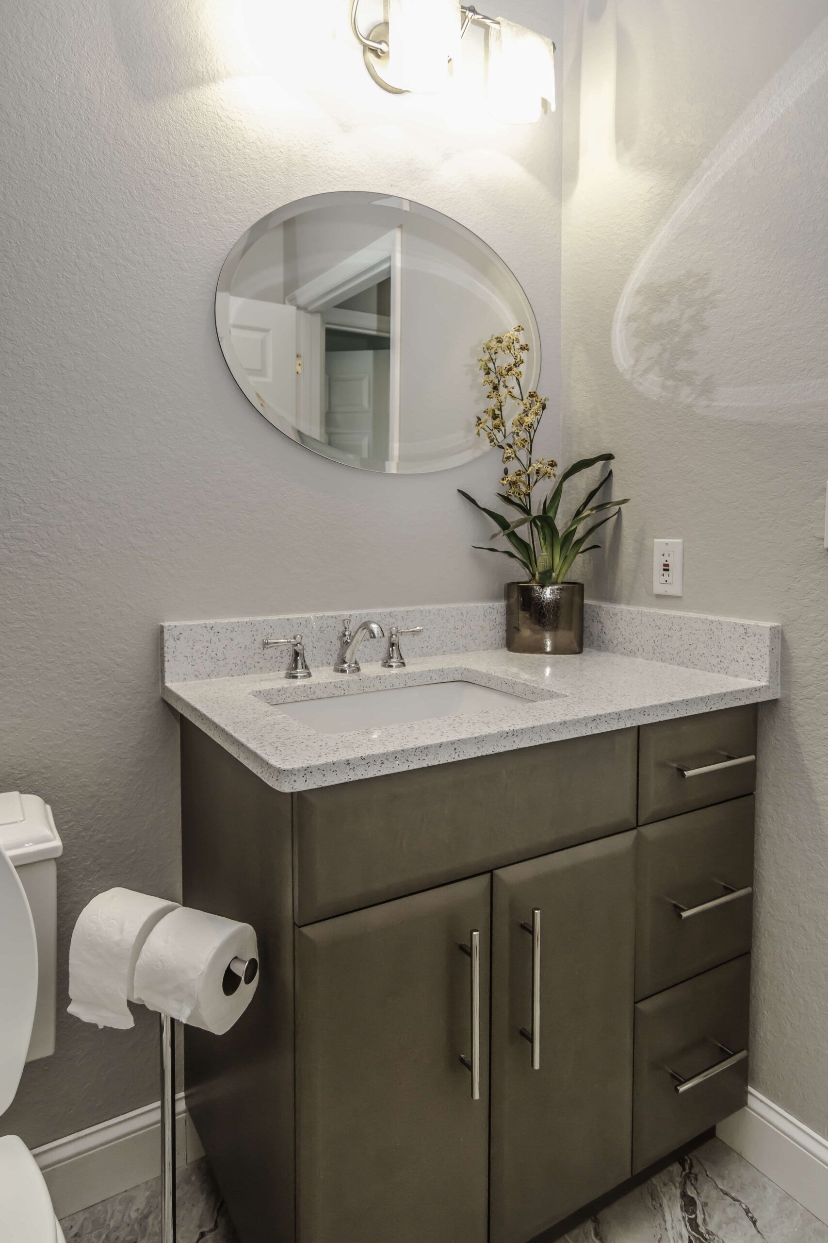 Small bathroom vanity with sink, round mirror, and potted plant on a speckled countertop.