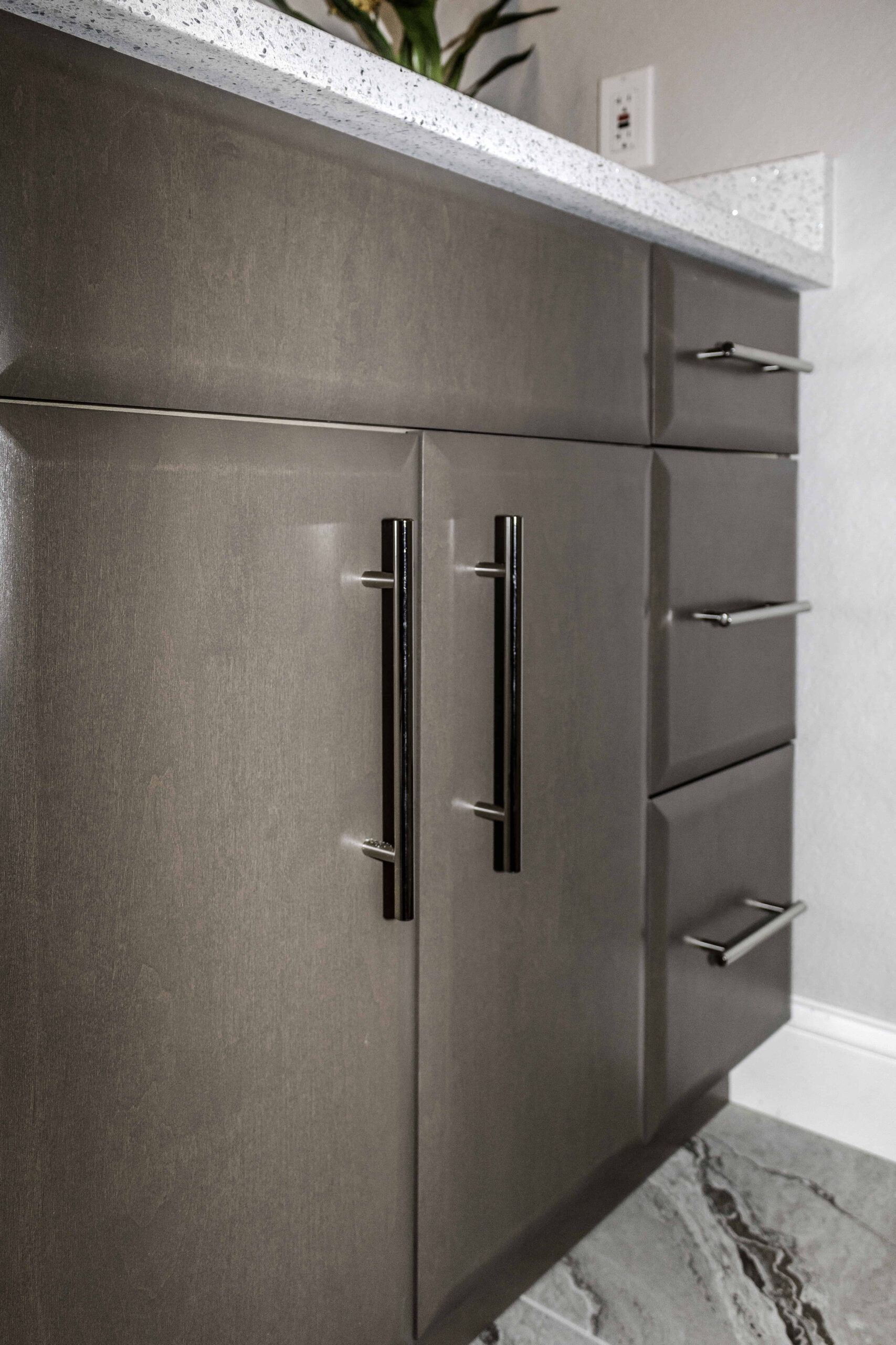 Dark gray kitchen cabinet with stainless handles and white countertop in a corner.